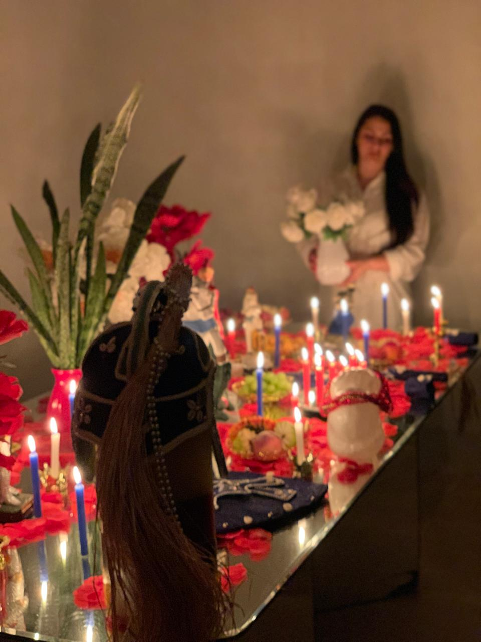 Altar com dezenas de velas acesas, flores vermelhas e imagens sagradas preparado para o trabalho amoroso